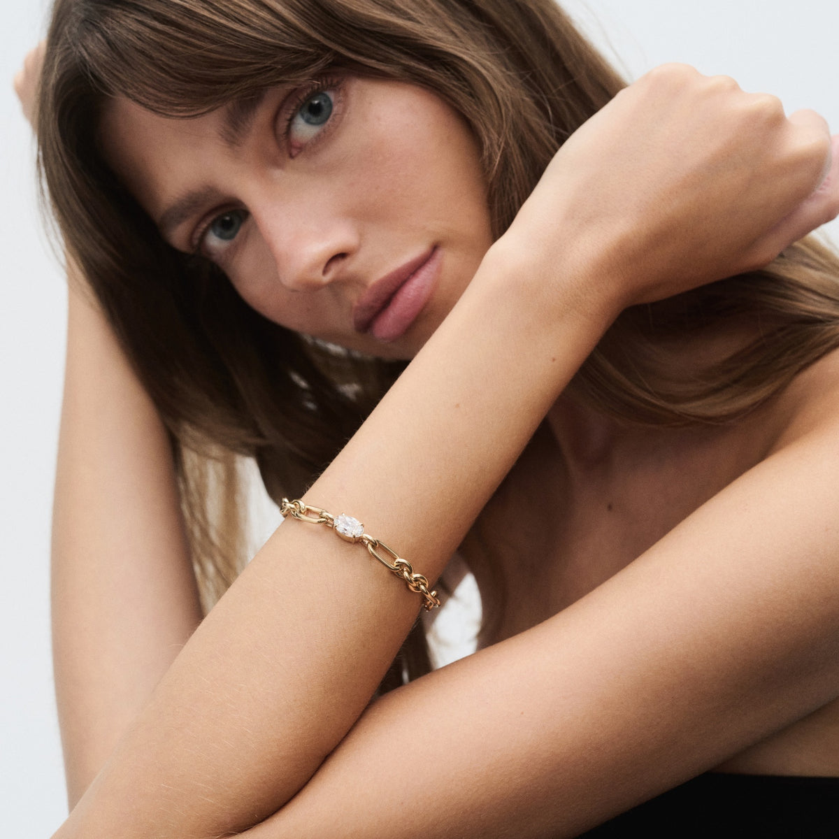 Woman with long hair wearing elegant gold bracelet, close-up. Minimalistic style, highlighting luxury jewellery. Neutral background.
