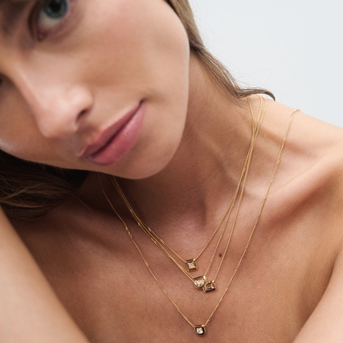Model wearing layered gold necklaces with elegant square pendants, showcasing high-end luxury jewellery against a soft-focus background.