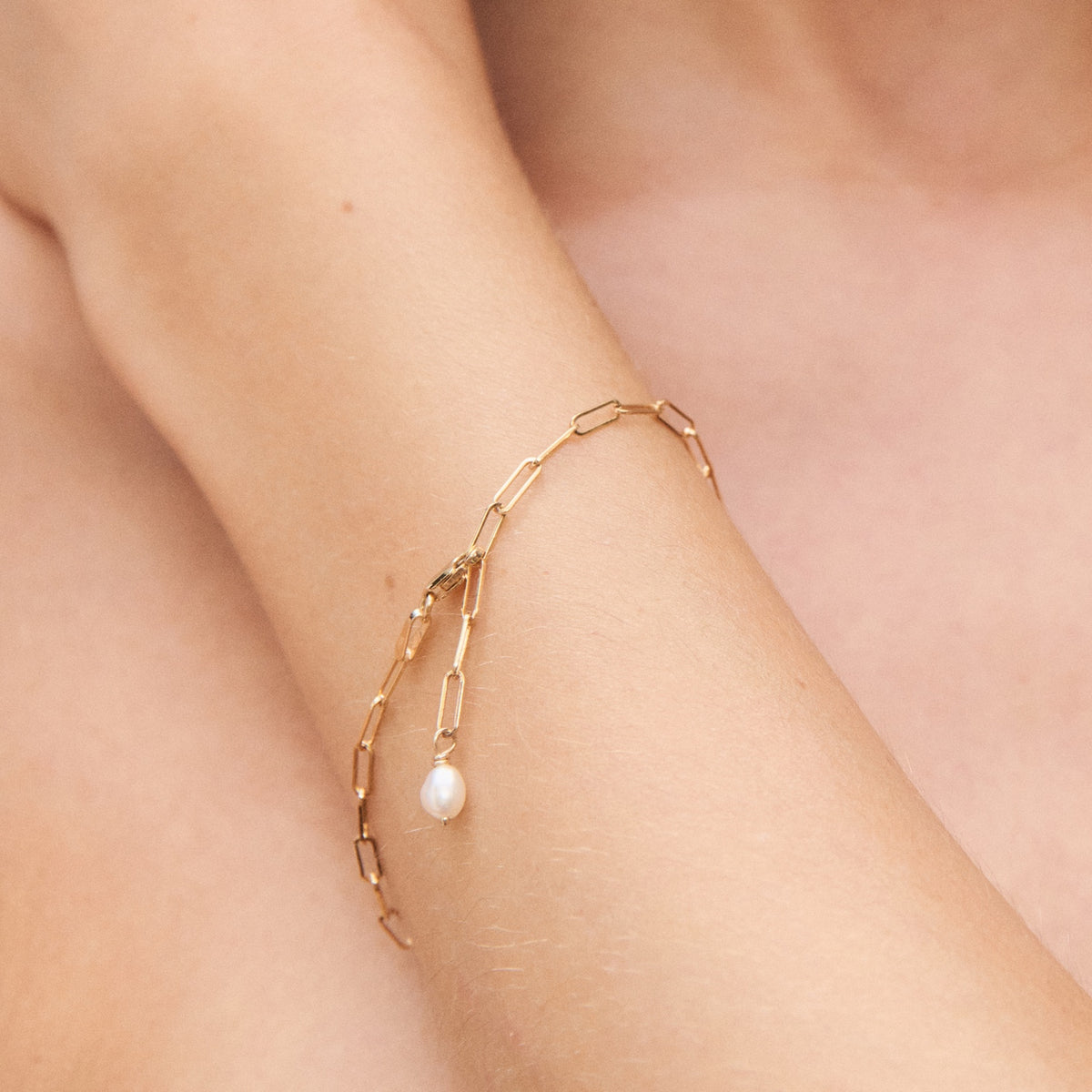 Elegant gold chain bracelet with small pearl detail, worn on wrist. Luxurious, minimalist design perfect for high-end jewellery enthusiasts.