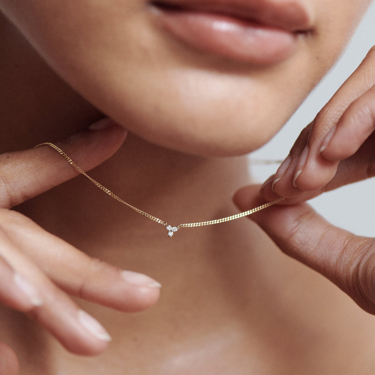 Close-up of a person holding a delicate gold necklace with a small diamond pendant, showcasing luxury jewellery.