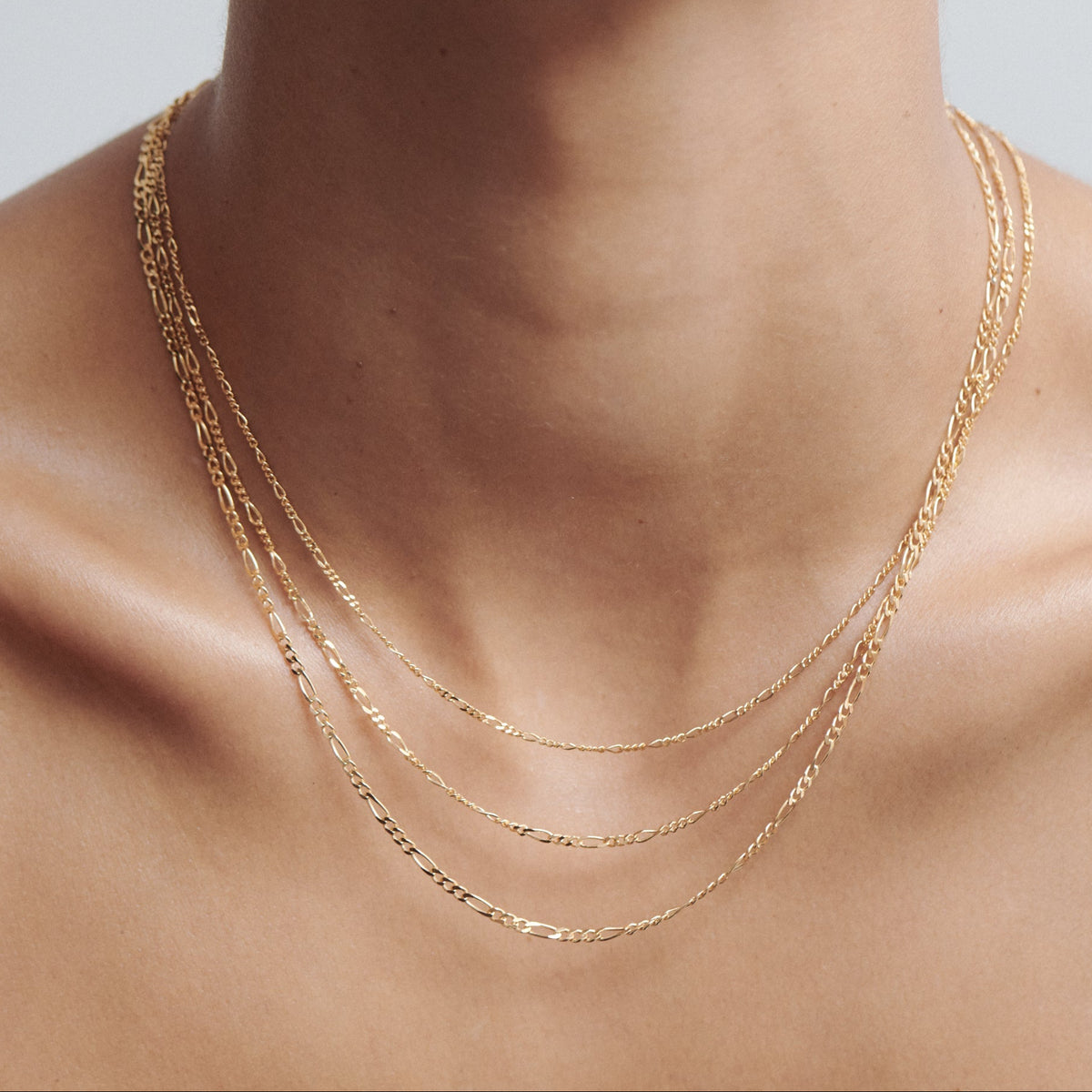 Close-up of a person wearing three delicate gold chains layered elegantly around the neck, showcasing luxury jewellery fashion.[text overlay: Small, Medium & Large (top to bottom)]