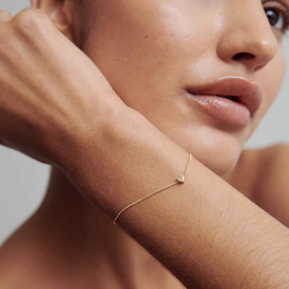 Close-up of a woman's wrist adorned with a delicate gold chain bracelet featuring a small geometric charm, showcasing luxury jewellery elegance.
