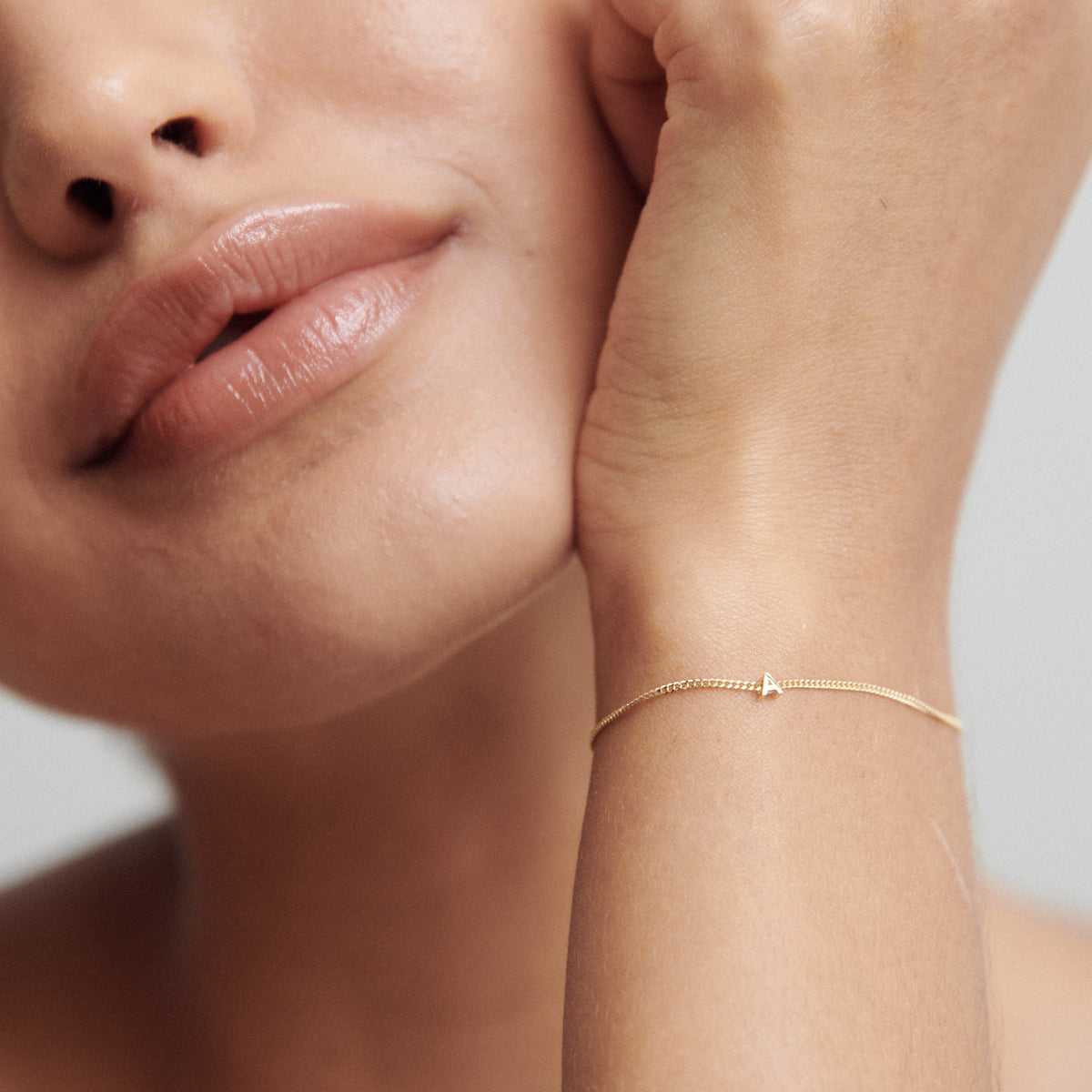 Close-up of a woman showcasing a minimalist gold bracelet with a small triangle charm, emphasising luxury jewellery and elegance.
