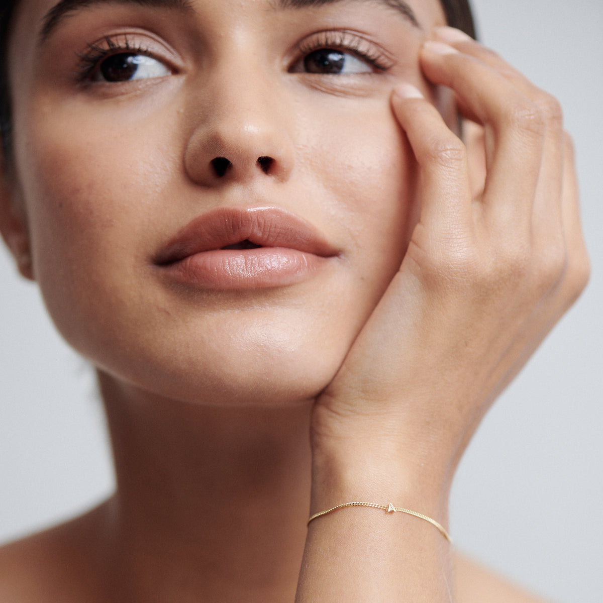 Woman with a serene expression wearing a delicate gold bracelet, resting her hand on her cheek, showcasing luxury jewellery elegance.