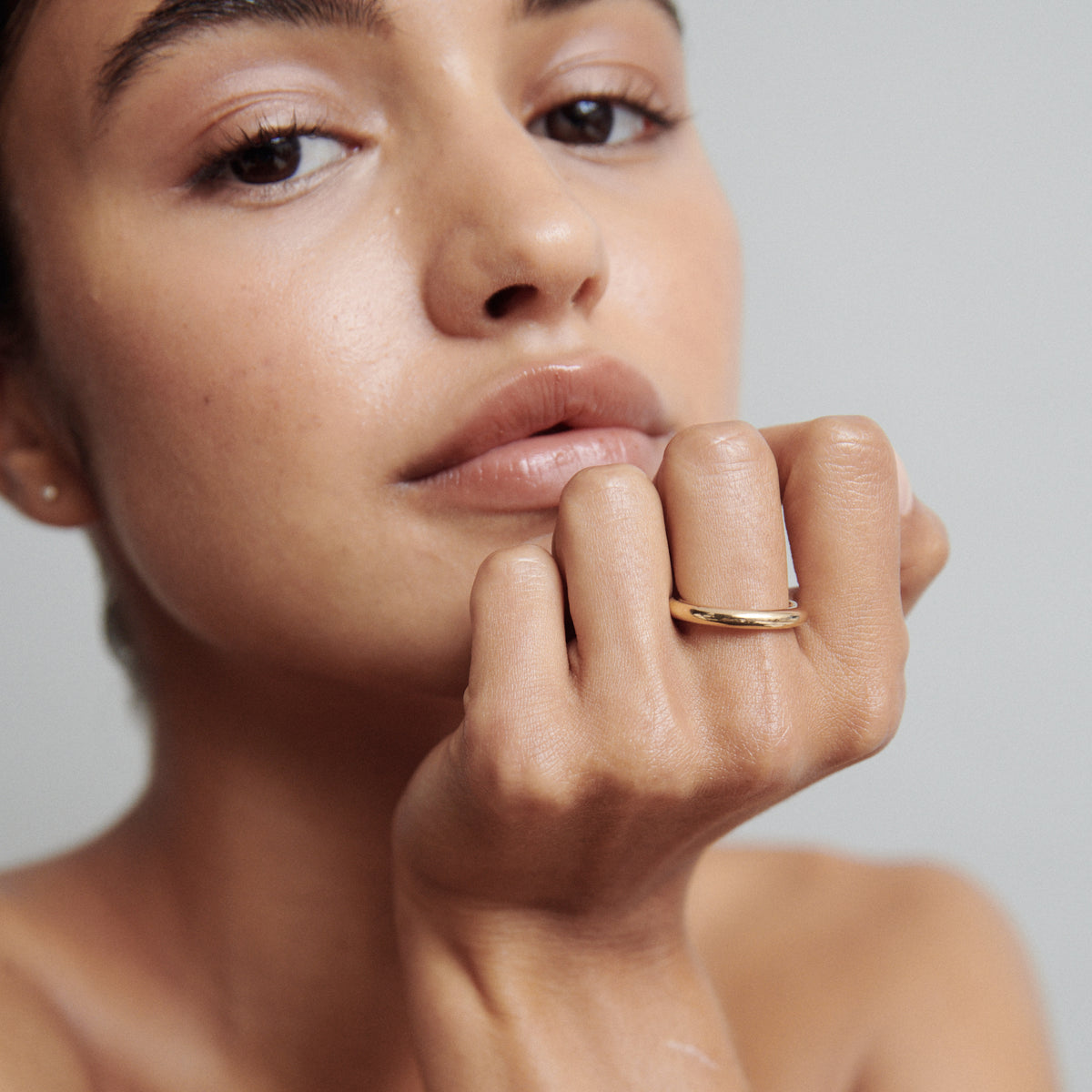 Woman with a minimalist gold ring on her hand, softly resting against her face. Luxurious, elegant jewellery style.
