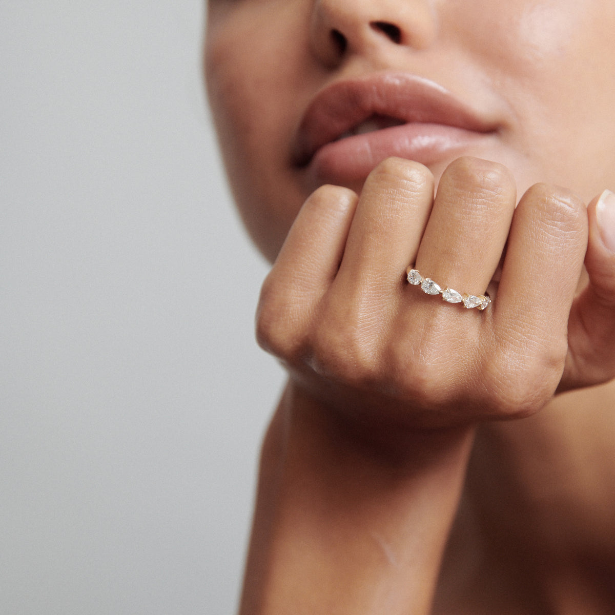 Close-up of a delicate gold ring with pear-shaped diamonds on a model's hand, showcasing luxury jewellery elegance.