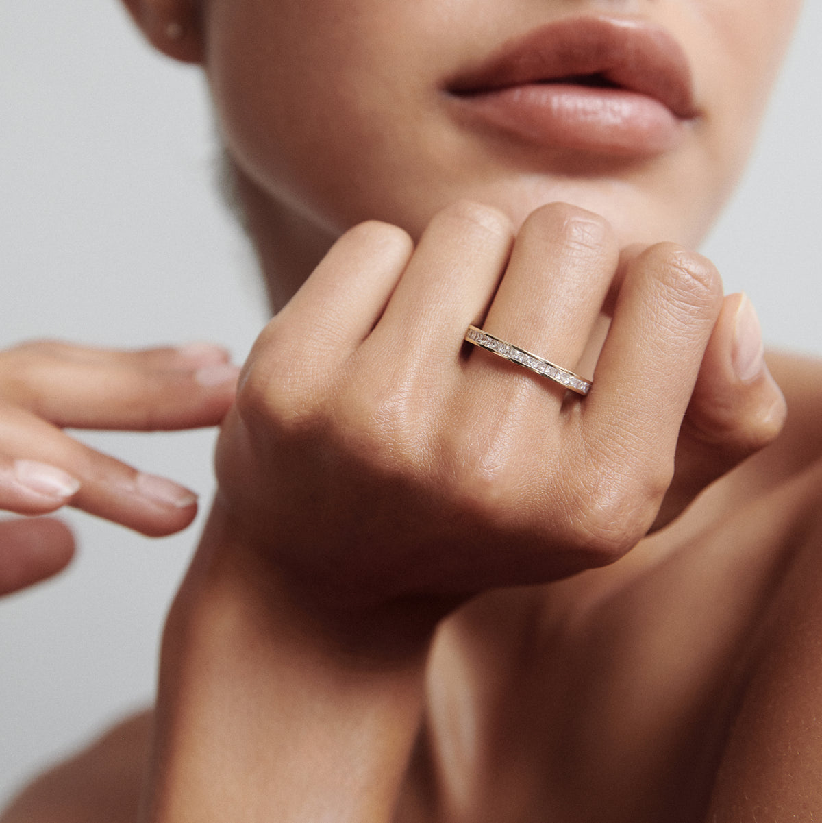 Close-up of a woman's hand wearing a thin diamond-encrusted gold ring. The focus is on the jewellery against a soft, neutral background.