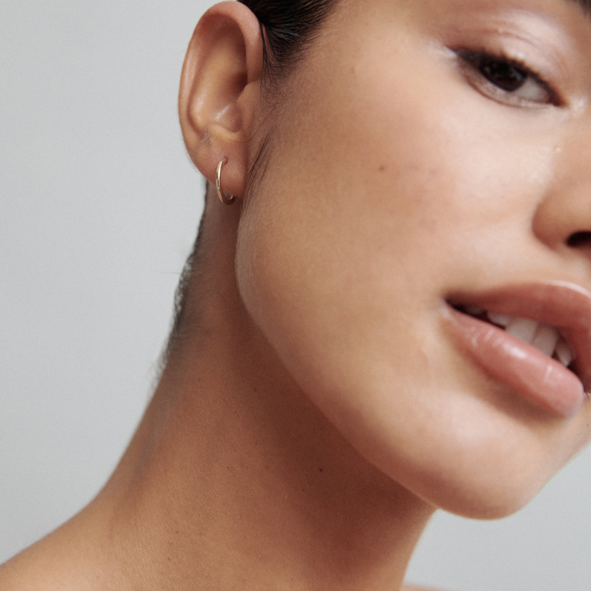 Close-up of a woman's face showcasing a minimalist gold hoop earring, highlighting luxury jewellery detail against a soft, neutral background.