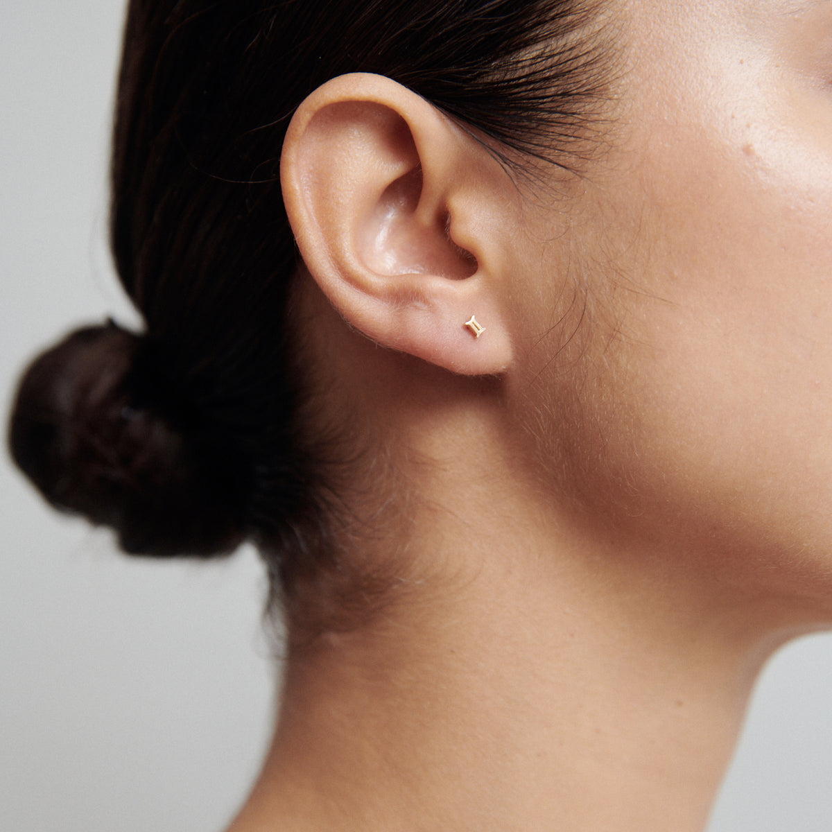 Close-up of a woman's ear with a minimalist gold star stud earring. Hair tied back, showcasing luxury jewellery elegance.