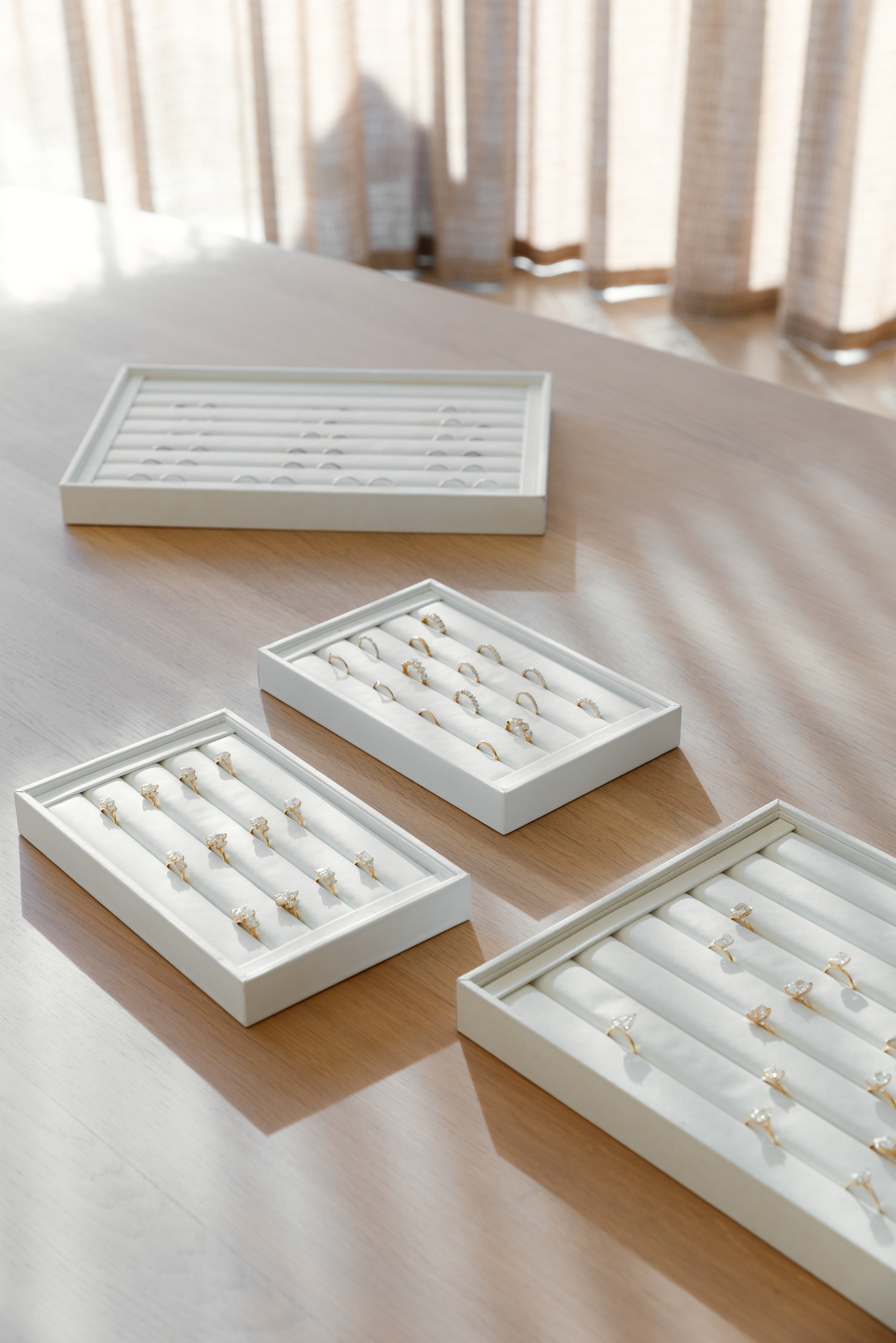 Four white jewelry trays with rings on a wooden surface.