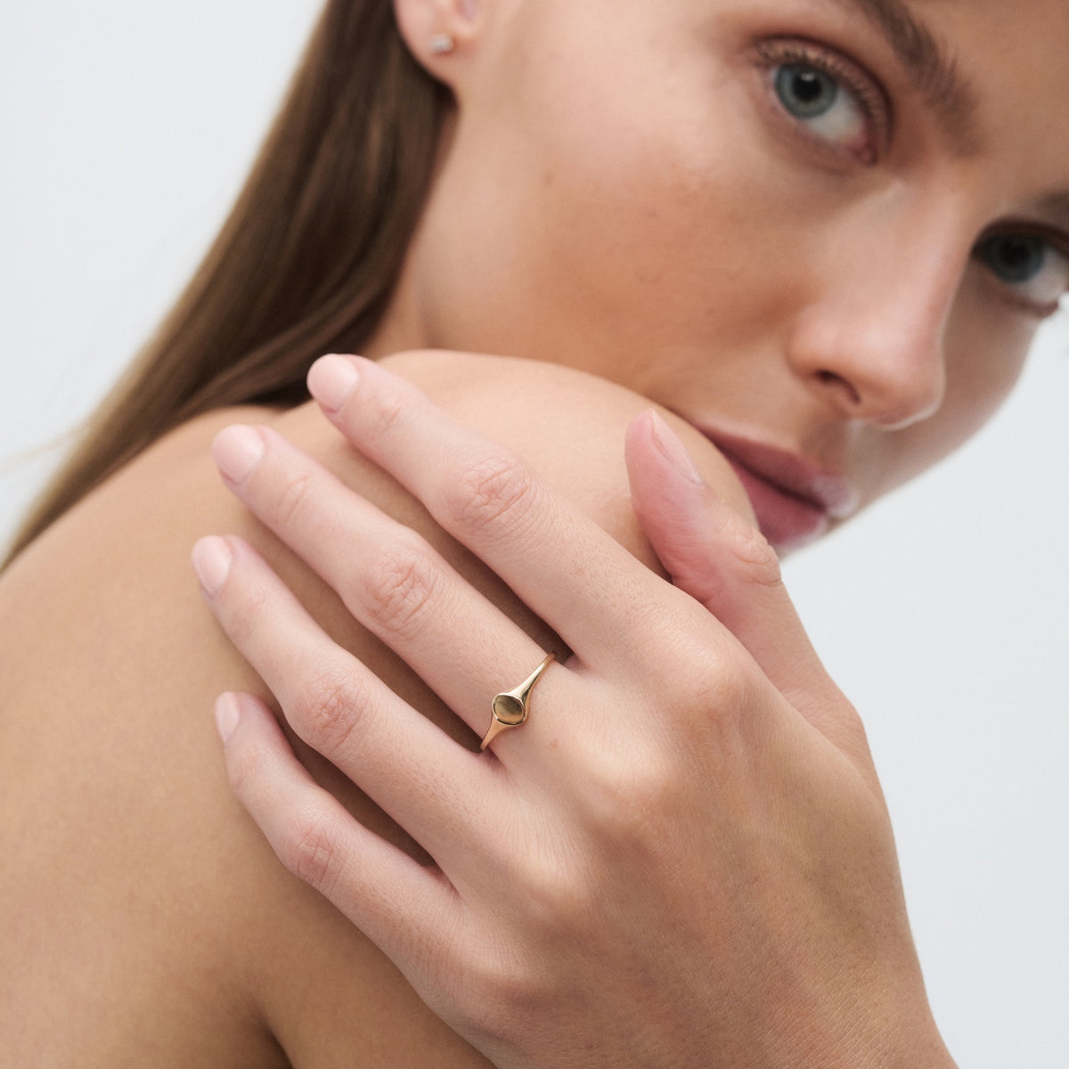 Woman showcasing a delicate gold ring on her finger, highlighting luxury jewellery. Her expression is serene against a minimalistic background.