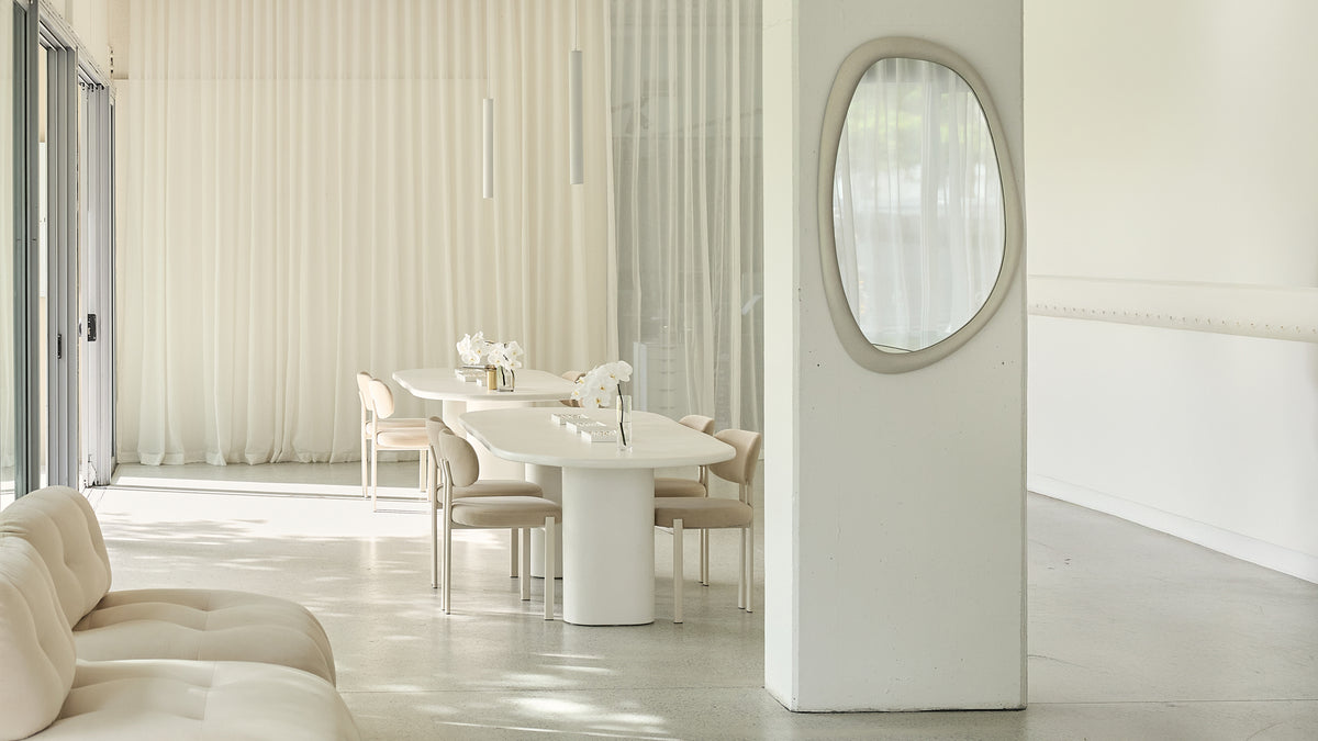 Elegant luxury showroom with minimalist white decor, a plush sofa, and a sleek dining table with modern chairs. Perfect for showcasing high-end jewellery.