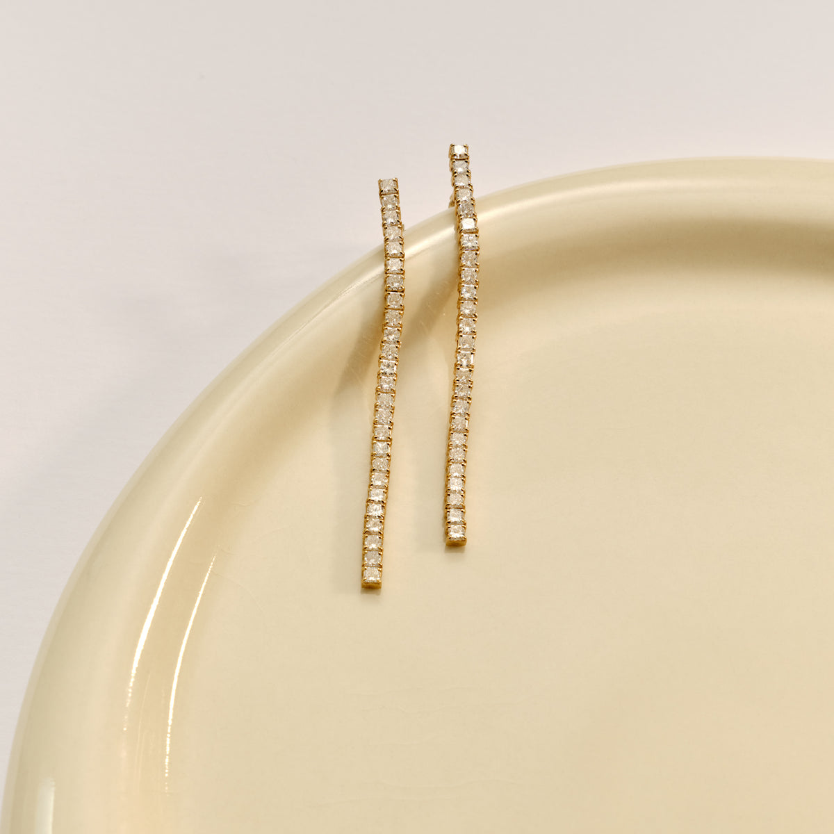 Elegant gold drop earrings with rows of sparkling diamonds, displayed on a pale, glossy ceramic surface. Luxurious jewellery.