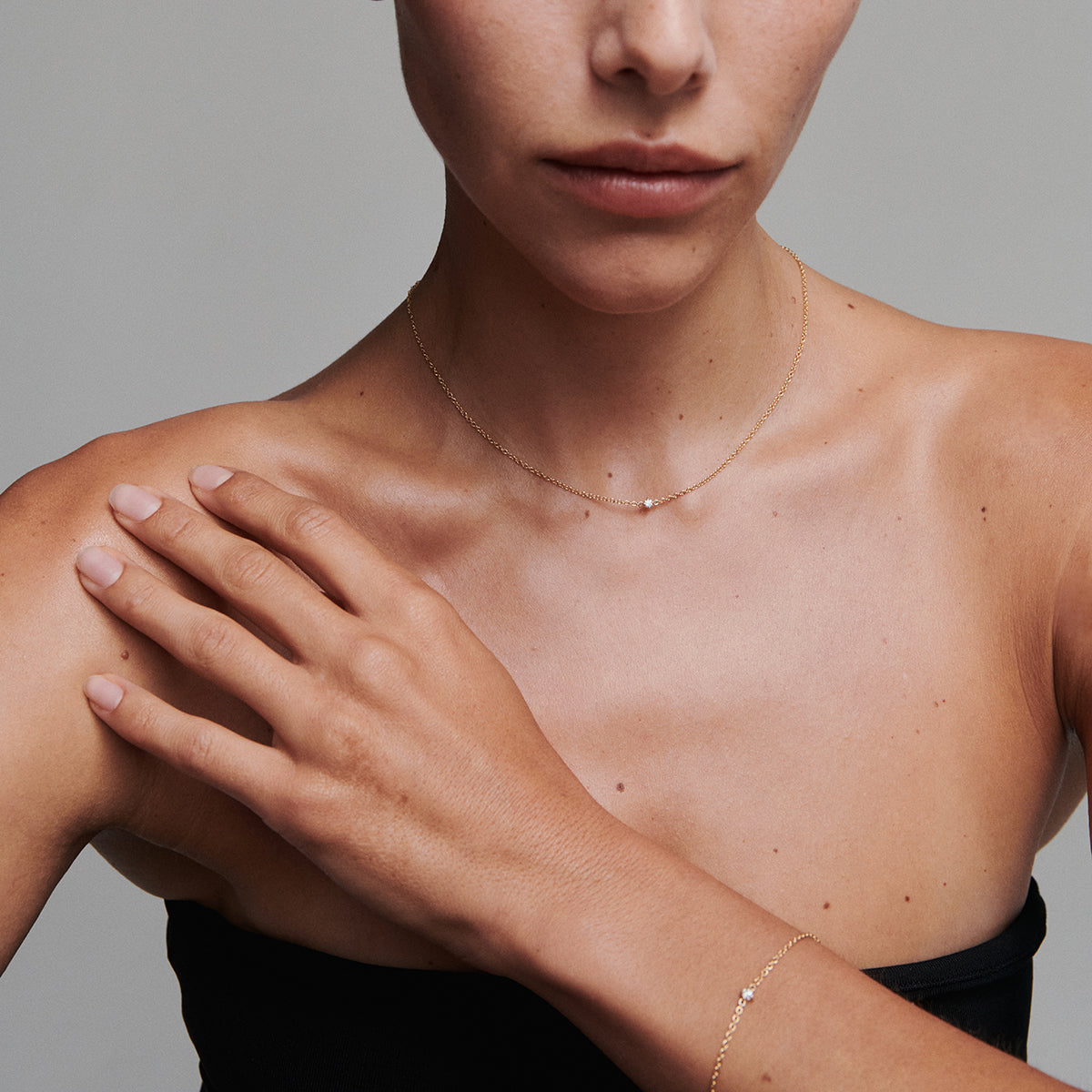Close-up of a person wearing a delicate gold necklace with a small gemstone on a neutral background