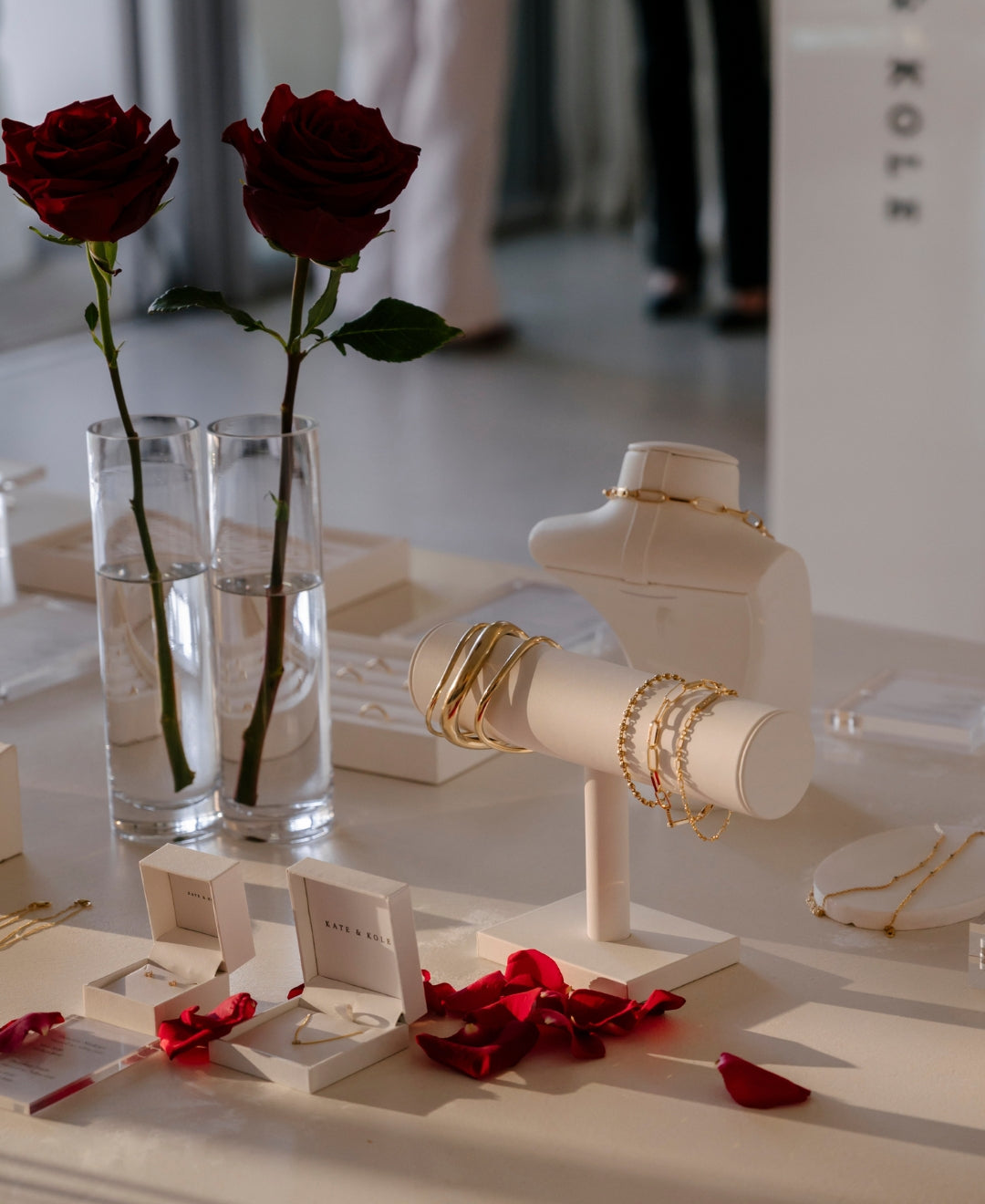 Luxurious jewellery display featuring gold bangles, necklaces, earrings, red rose petals, and vases with red roses, set on a chic table.