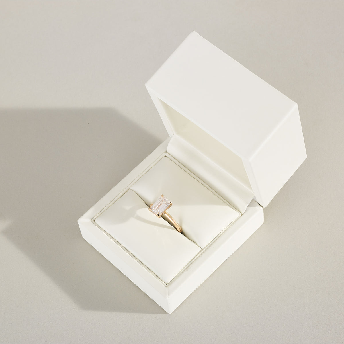 Diamond ring in an open white jewelry box on a light gray background
