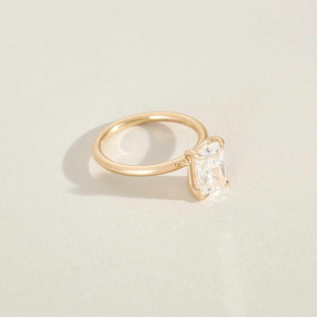 Gold ring with a cushion-shaped diamond on a light beige background