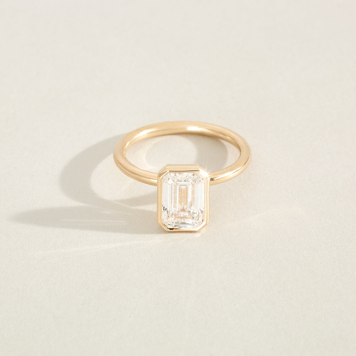 Gold ring with a rectangular diamond on a light beige background