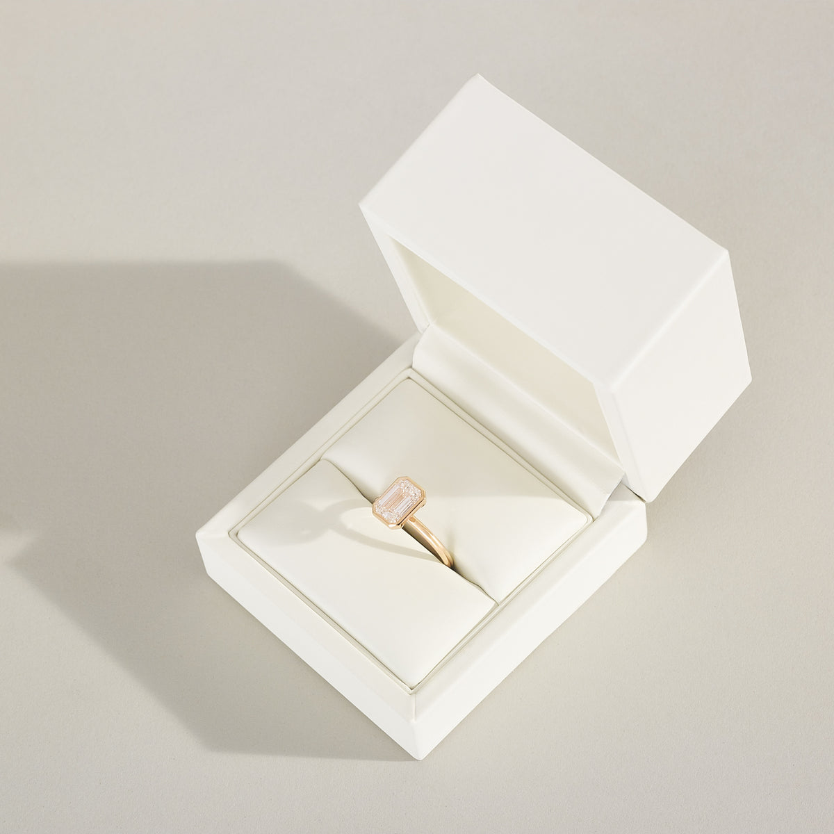 Gold ring in an open white jewelry box on a light gray background