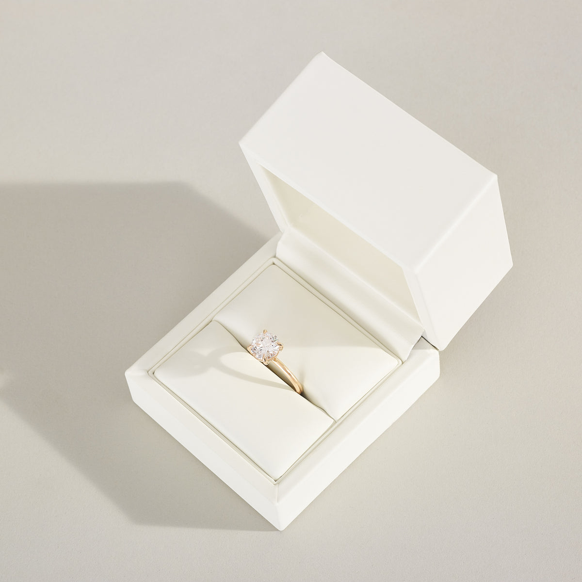 Open white jewelry box with a ring inside on a light gray background