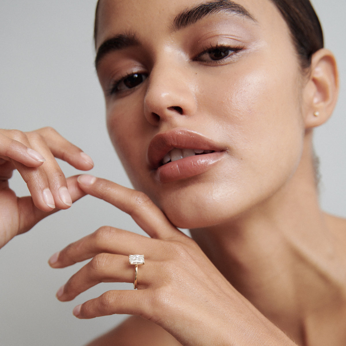 Woman showcasing luxury gold ring with large rectangular gemstone, posing gracefully. Appears polished and sophisticated.
