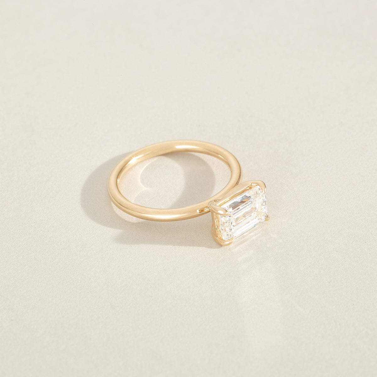 Gold ring with a rectangular diamond on a light beige background