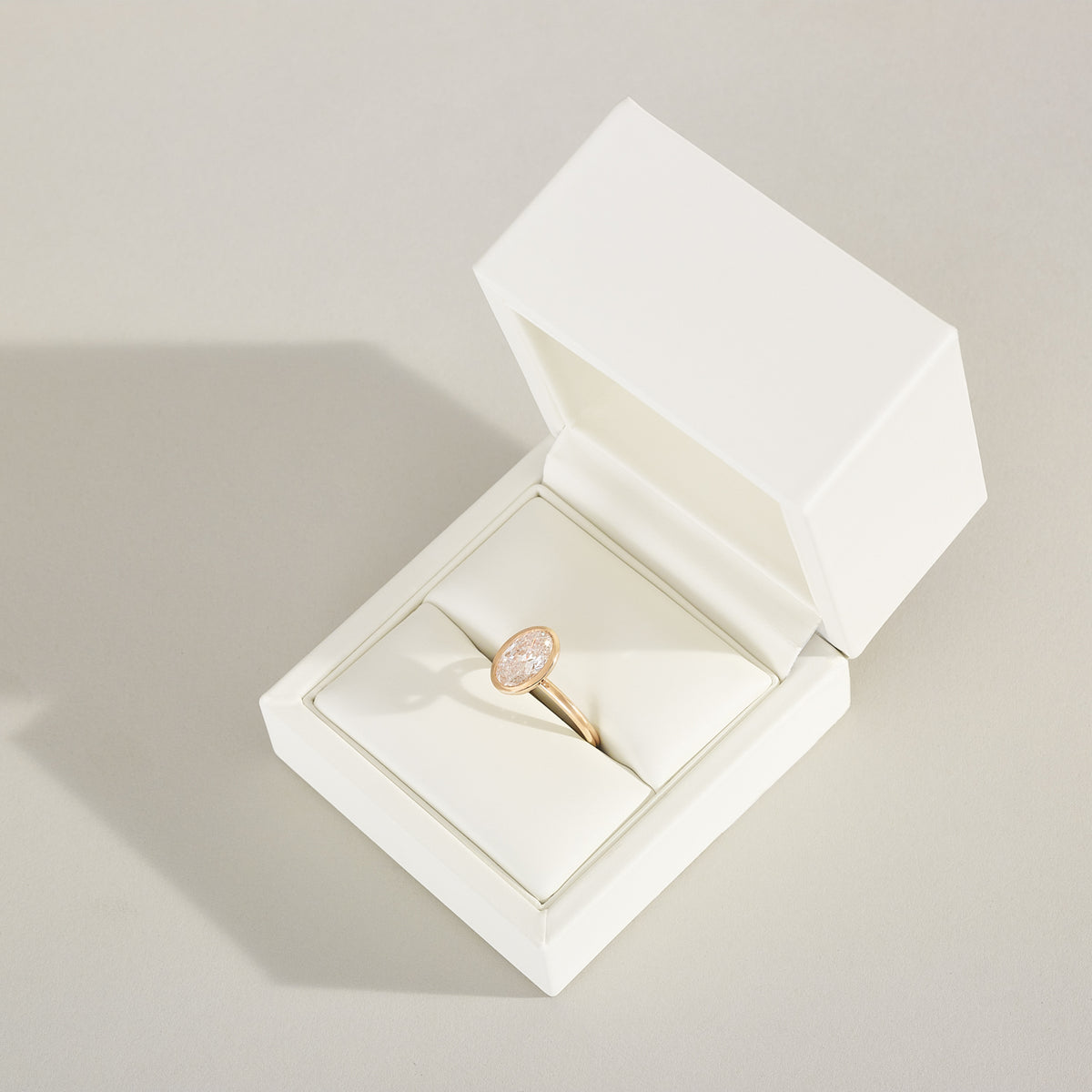 Gold ring with a diamond in an open white jewelry box on a light gray background