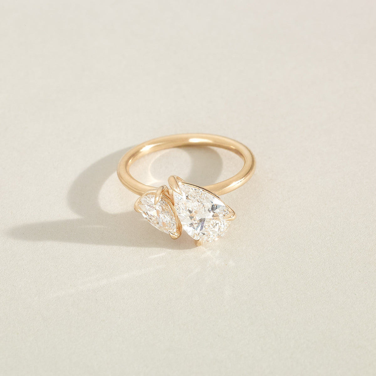Gold ring with two pear-shaped diamonds on a light beige background