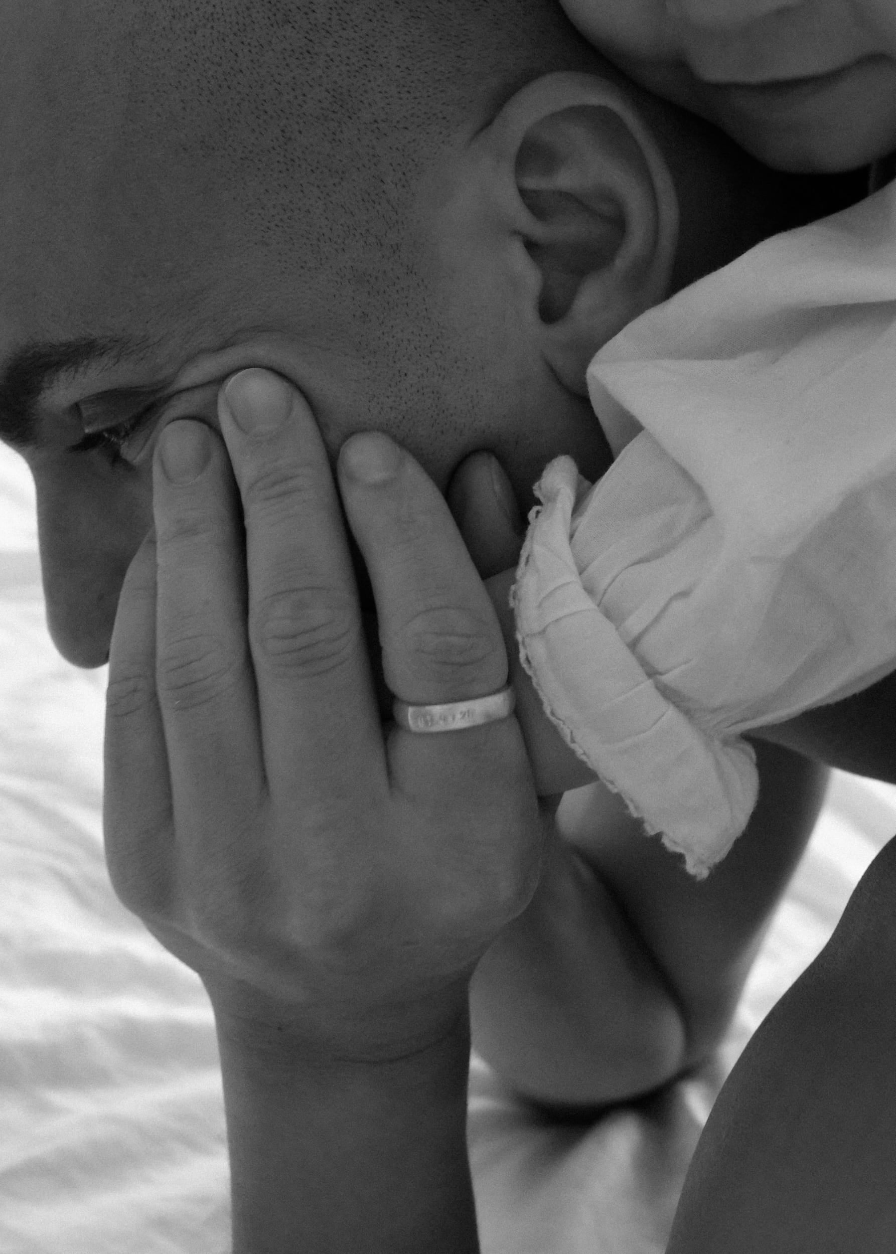 Black-and-white close-up of a daughter resting on top of her father, with an engraved Milestone Ring visible on his hand.