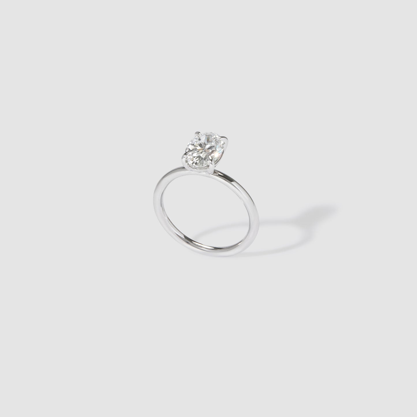 Solitaire diamond engagement ring with a round brilliant cut stone, set on a sleek platinum band; luxury jewellery on a grey background.
