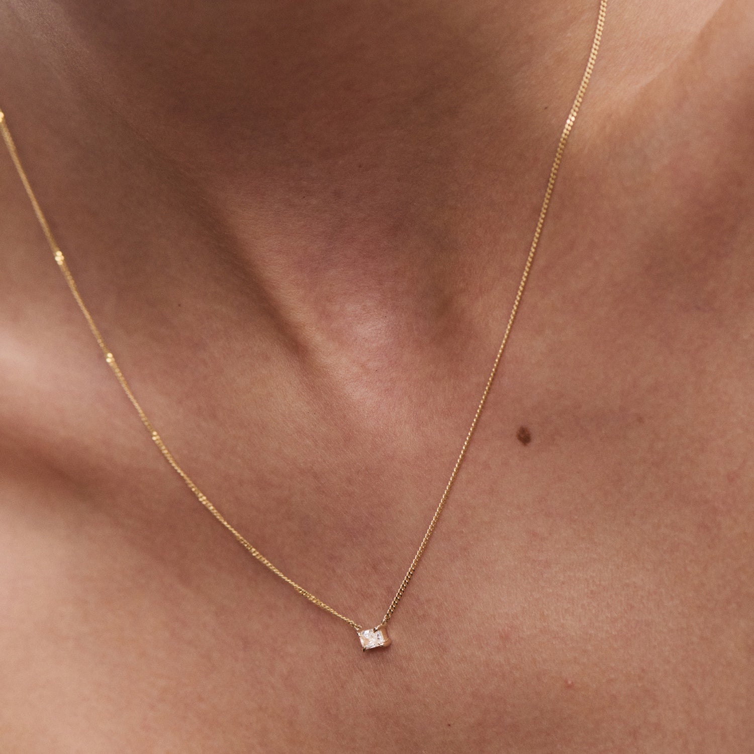 Close-up of a delicate gold necklace with a small, sparkling diamond pendant on a person's neck, symbolising luxury and elegance. [text overlay: Radiant] 