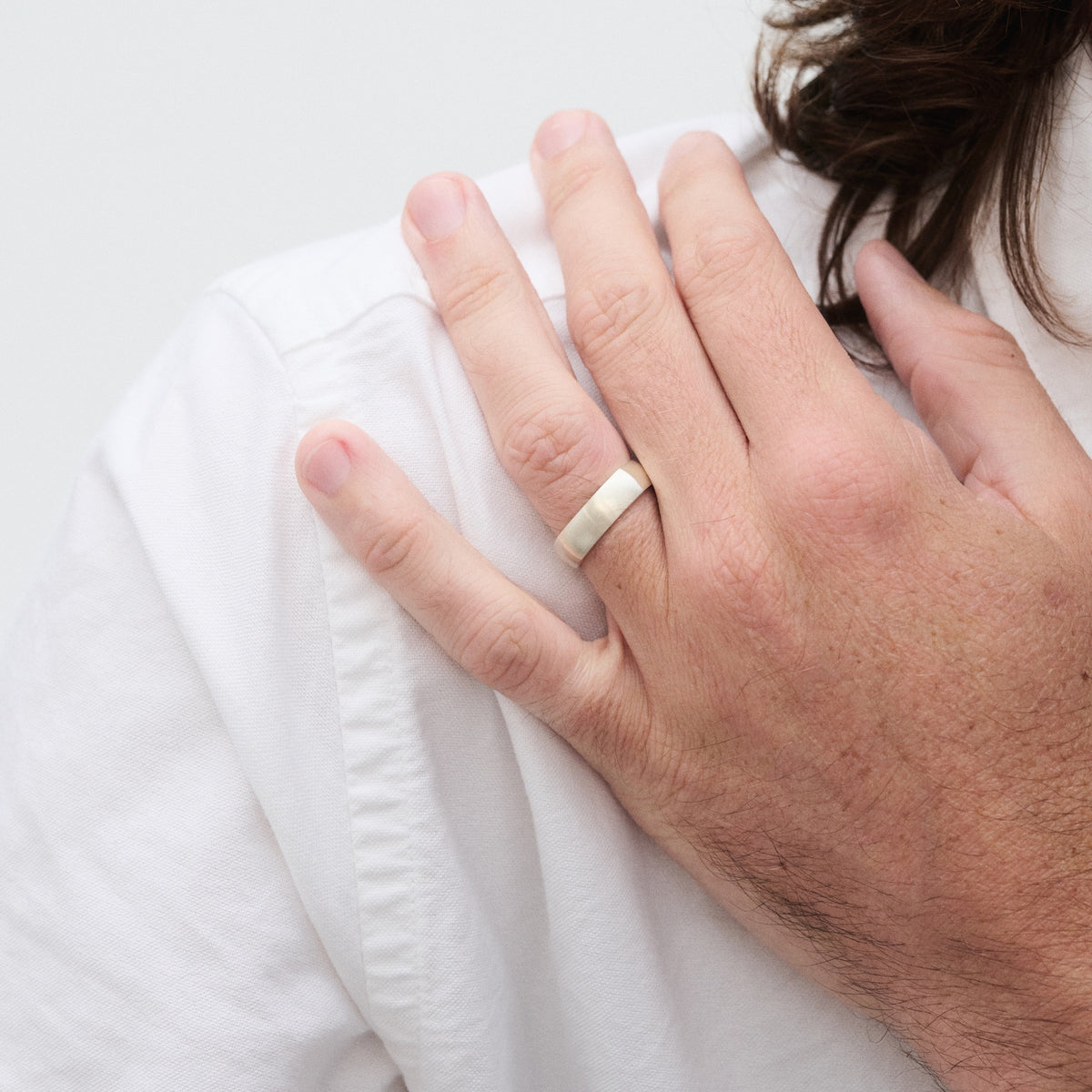 Man's hand wearing a white gold wedding band, resting on his chest against a white shirt, showcasing elegant and minimalist jewellery design.