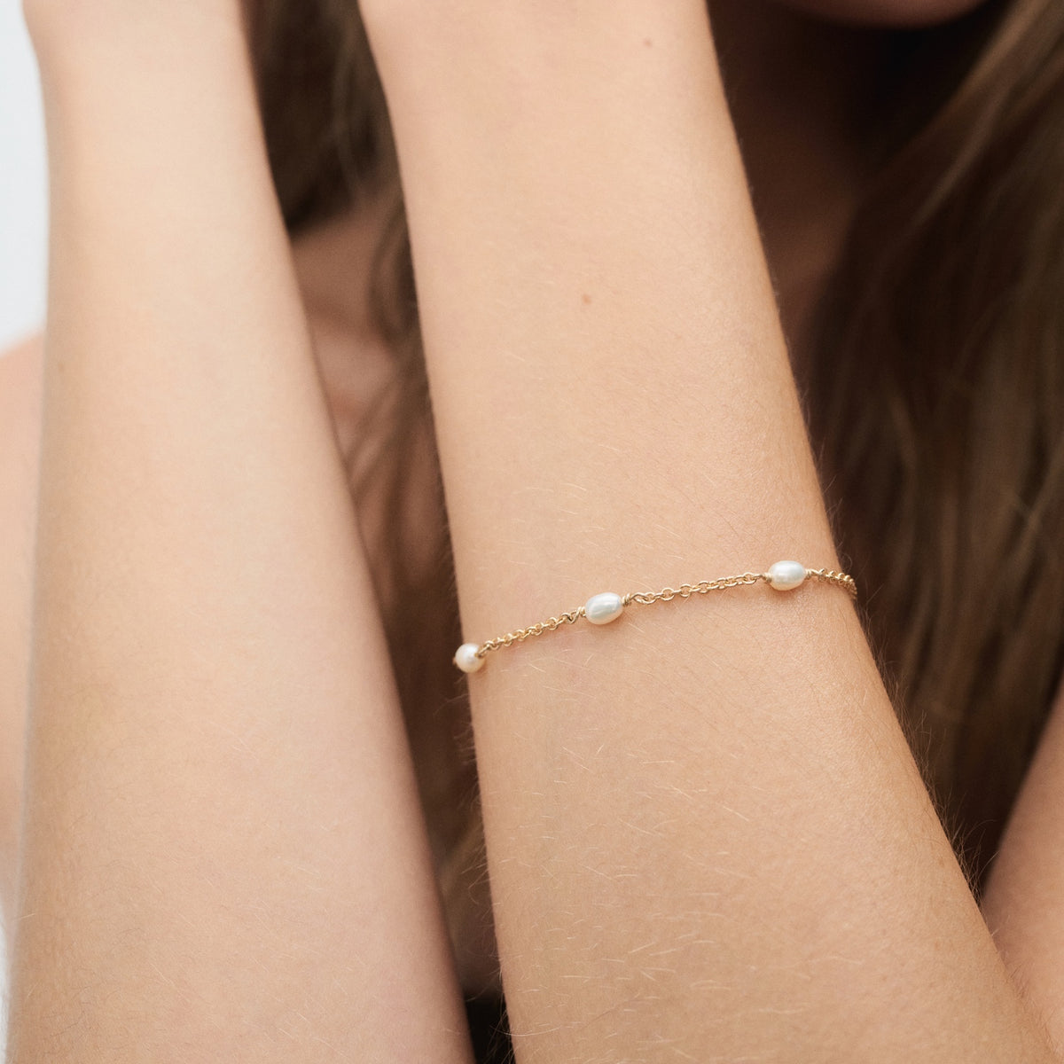 A gold bracelet with delicate pearls adorns a woman's wrist against a soft background, showcasing luxury jewellery elegance and style.