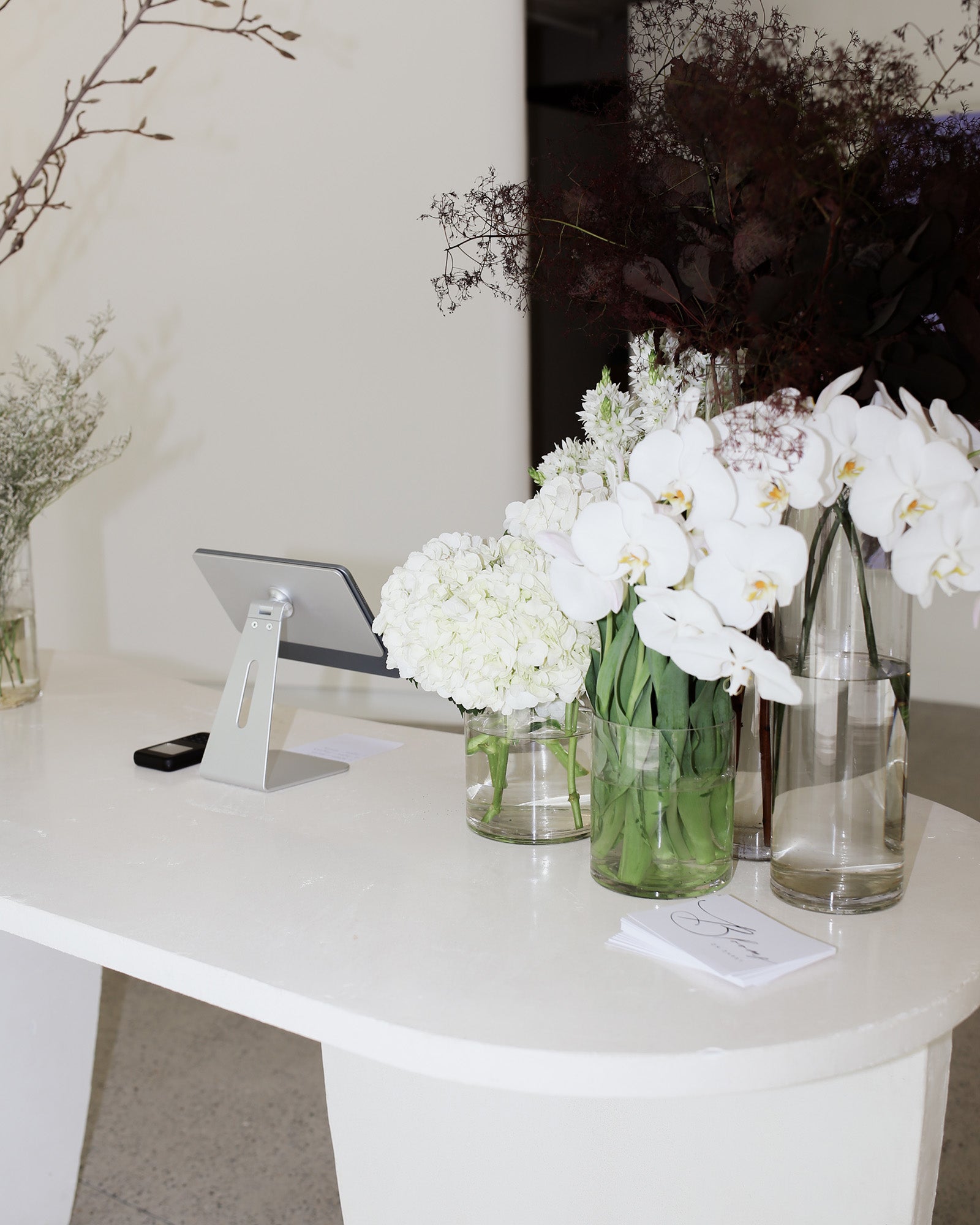 Elegant jewellery shop counter adorned with white orchids and hydrangeas in glass vases, next to a tablet stand, exuding luxury and style.