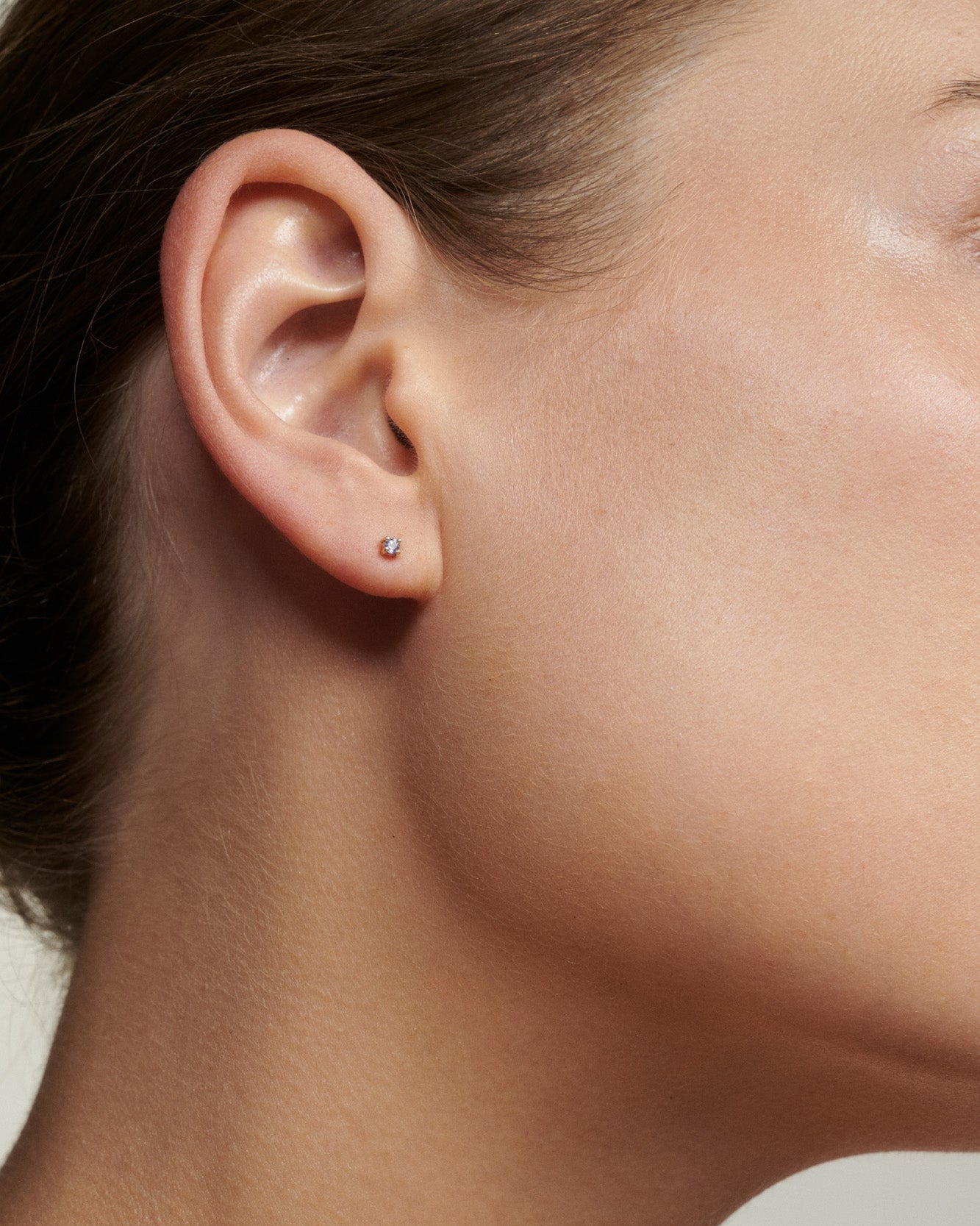 Close-up of a person wearing a small earring on a neutral background [text overlay: Alexandrite]