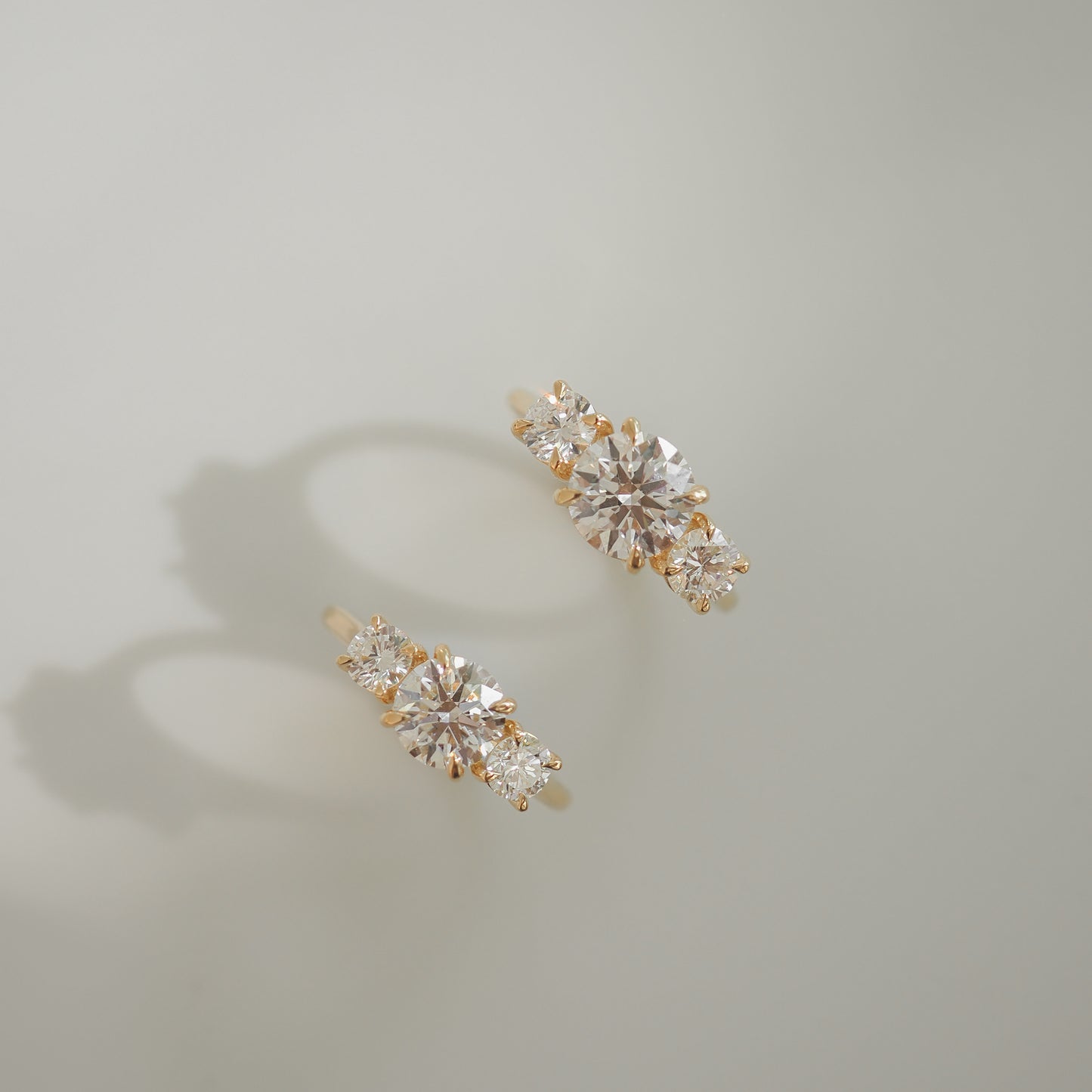 Gold earrings with sparkling round and marquise-cut diamonds, casting soft shadows on a light grey background. Luxurious and elegant design.