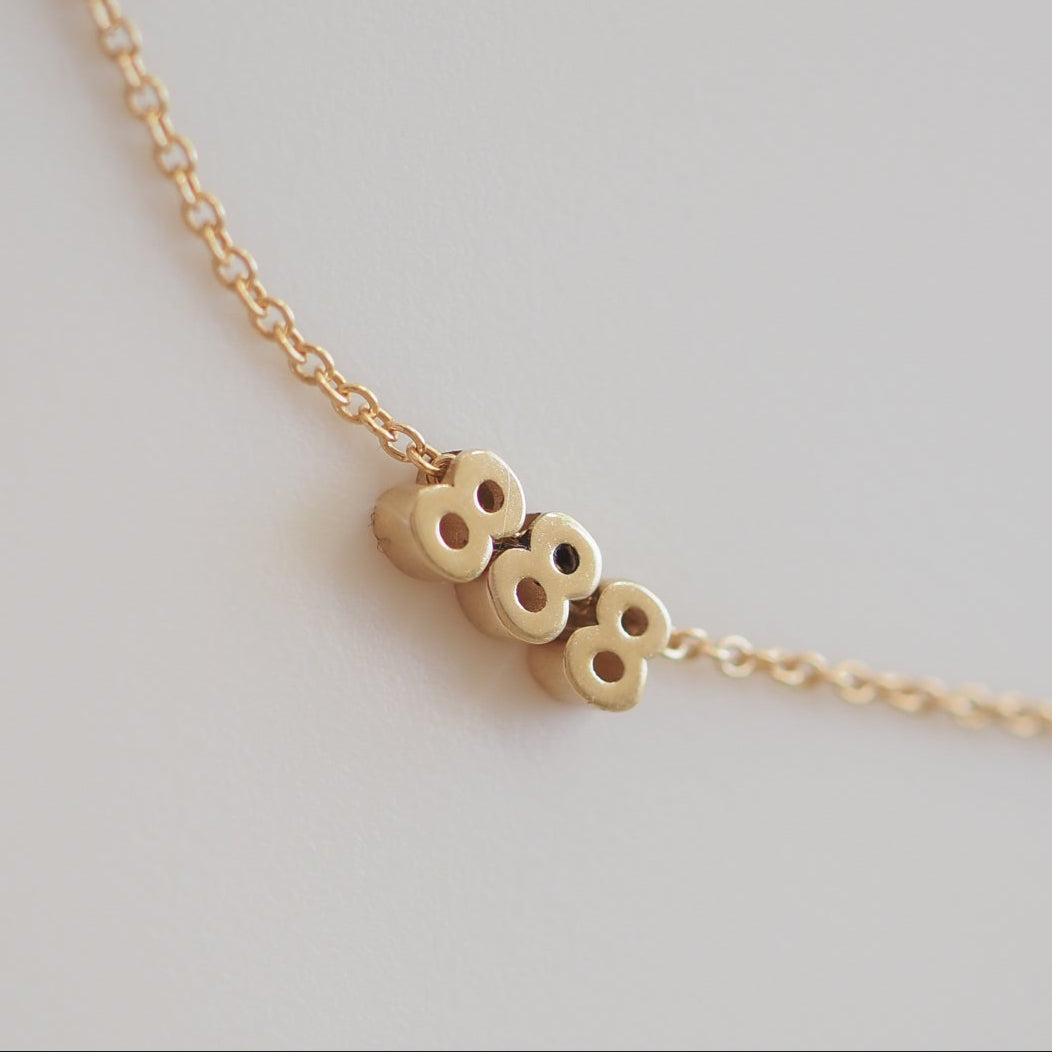 Gold necklace with three '8' charms on a delicate chain, showcasing minimalist luxury jewellery design.