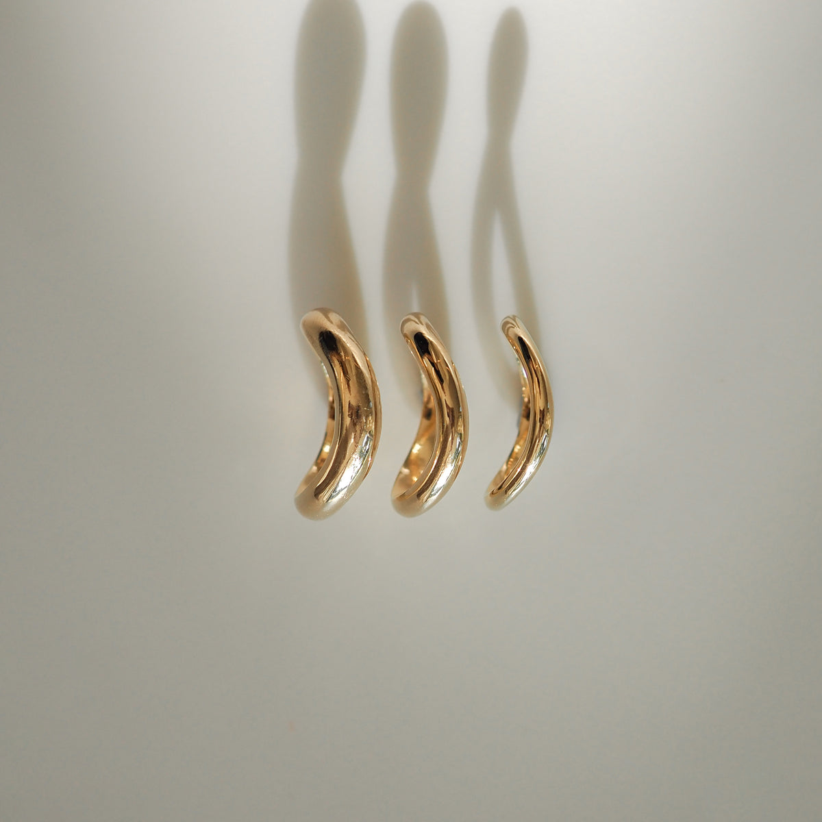 Three elegant, gold, crescent-shaped pendants casting soft shadows on a light background. Perfect for luxury jewellery enthusiasts.