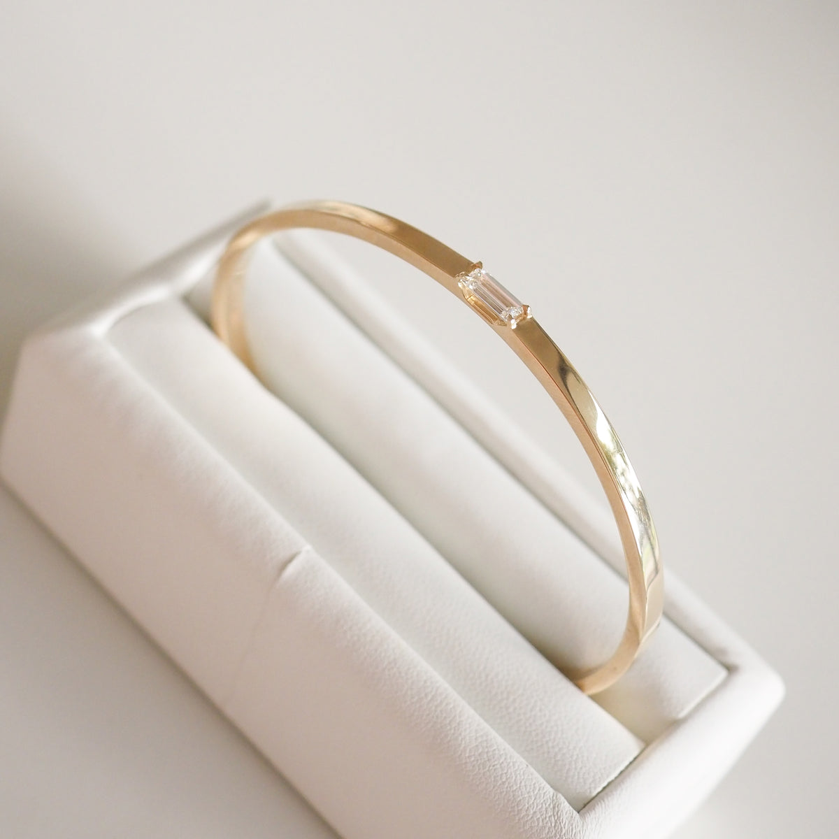 Gold bangle with a rectangular diamond, elegantly displayed on a white jewellery stand. Perfect for luxury fashion enthusiasts.