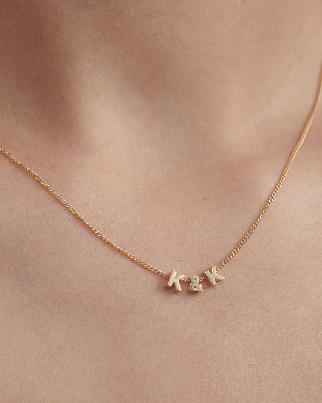 Gold necklace with Tiny Letters on a person's neck against a neutral background