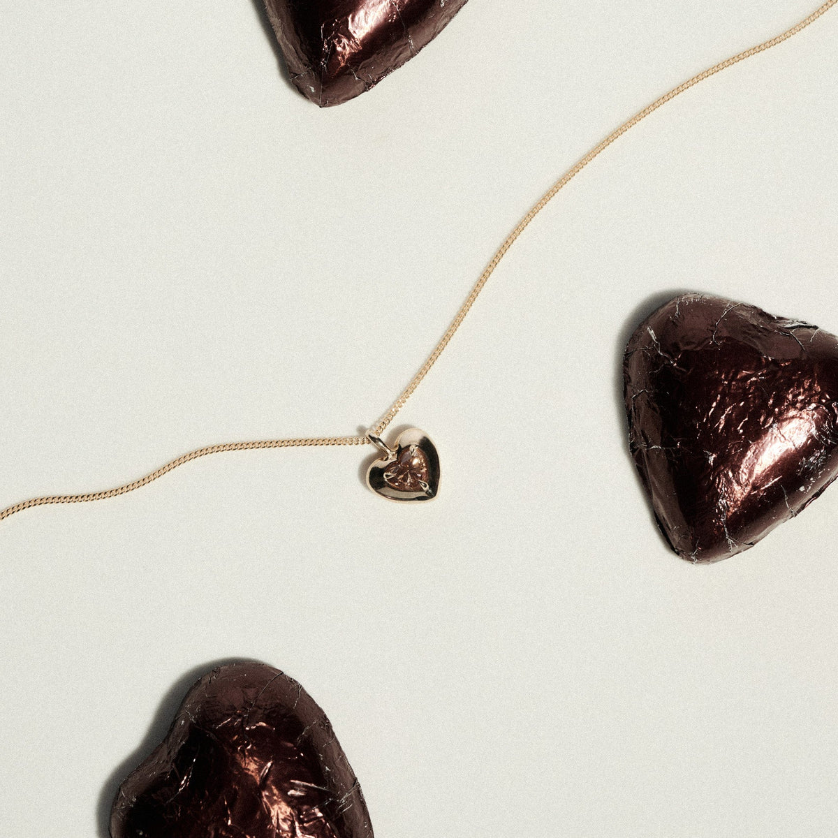 Heart-shaped chocolate pieces with a gold necklace draped on a light background