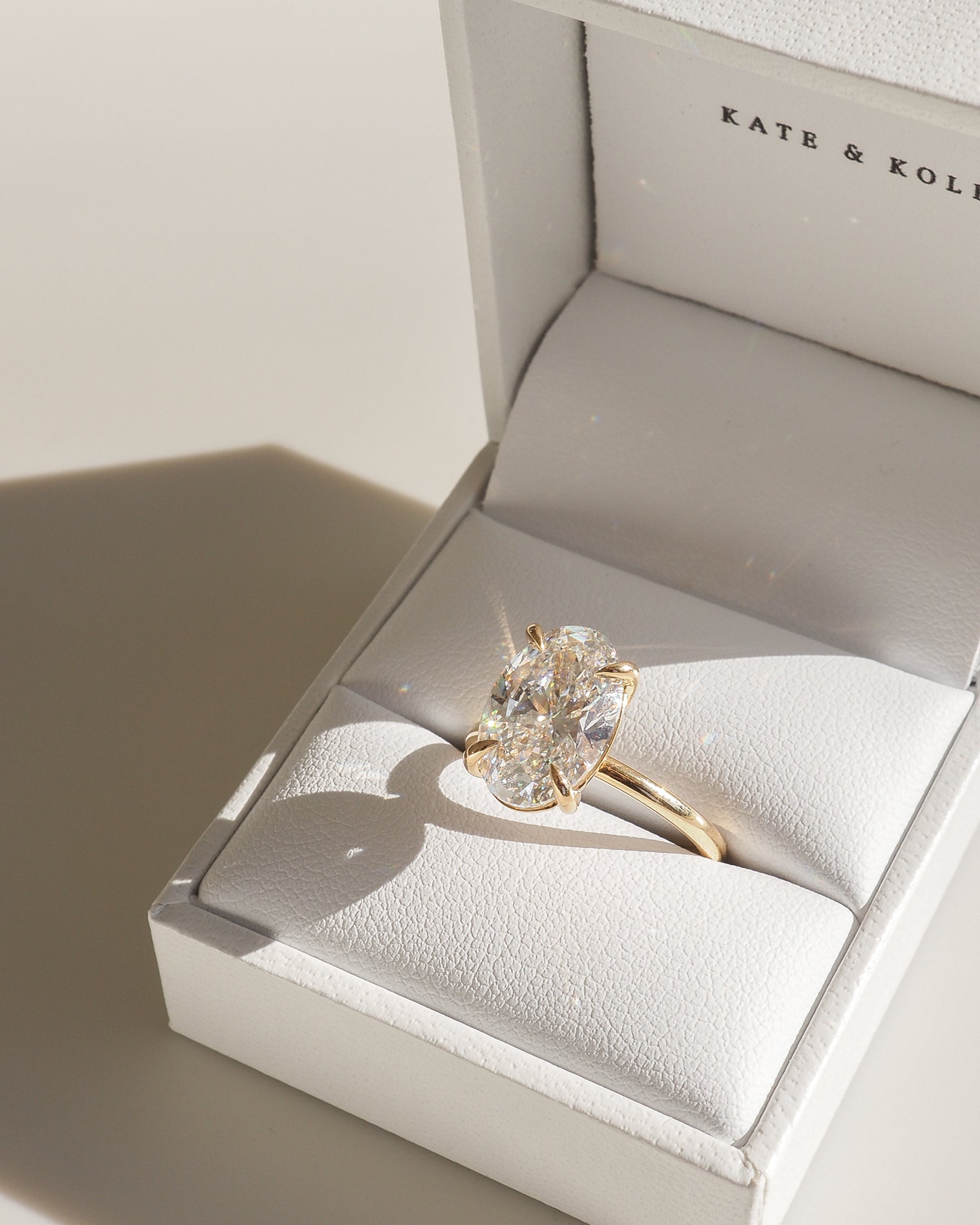Gold engagement ring with large oval diamond in an open white jewellery box, Kate & Kole branding visible.