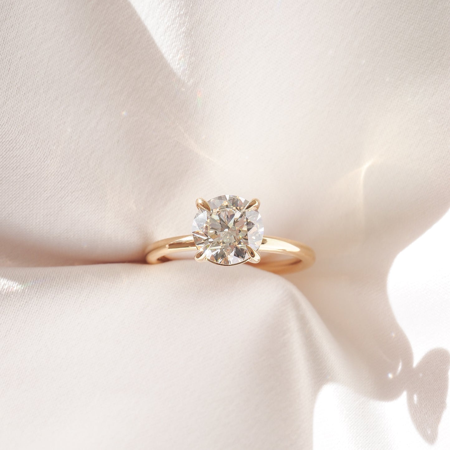 Gold solitaire engagement ring with a large round diamond, elegantly displayed on soft, white fabric, capturing luxury and romance.