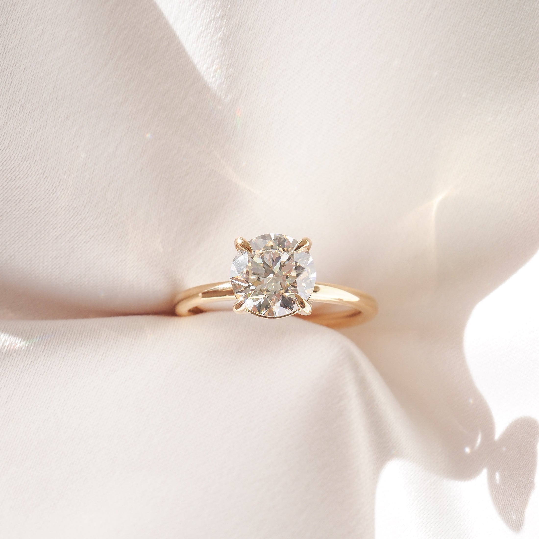 Gold solitaire engagement ring with a large round diamond, elegantly displayed on soft, white fabric, capturing luxury and romance.