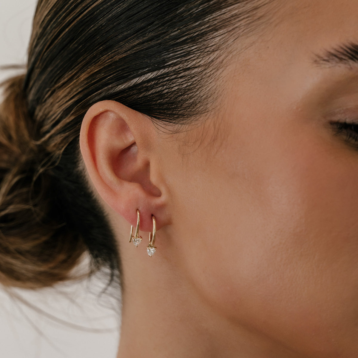 Close-up of a woman's ear wearing two gold hoop earrings; one features a small diamond drop, enhancing a luxury jewellery aesthetic.