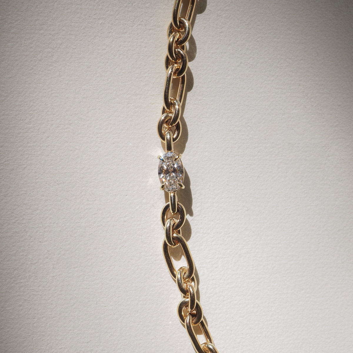 Gold chain with oval diamond link, elegant and minimalist luxury jewellery on a light background.
