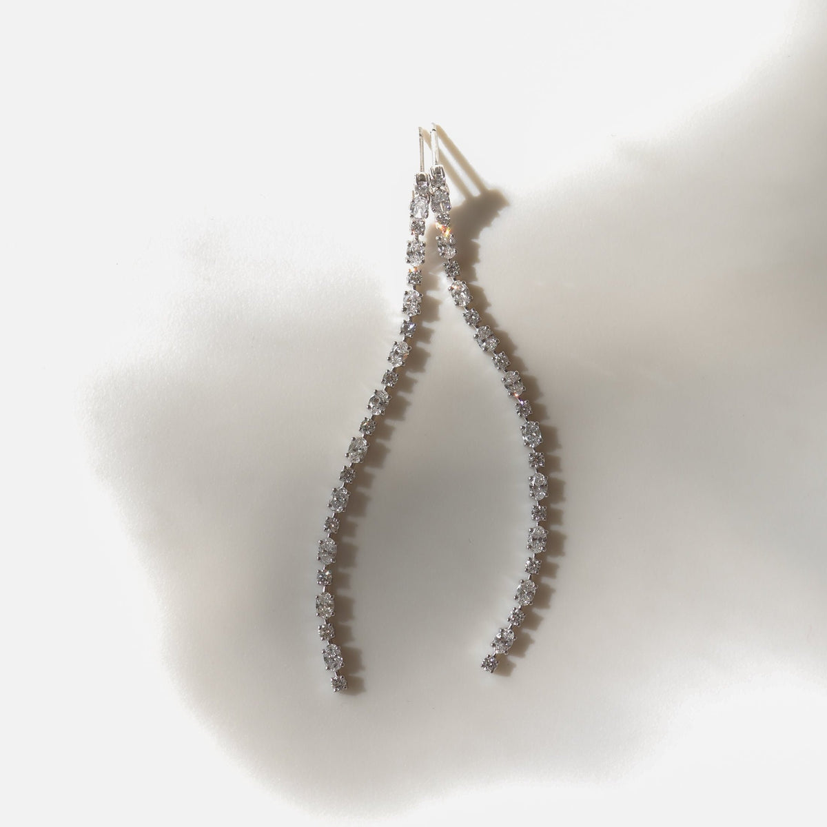 Elegant curved diamond earrings on a soft, diffused background, showcasing luxury jewellery design and sparkling gemstones.
