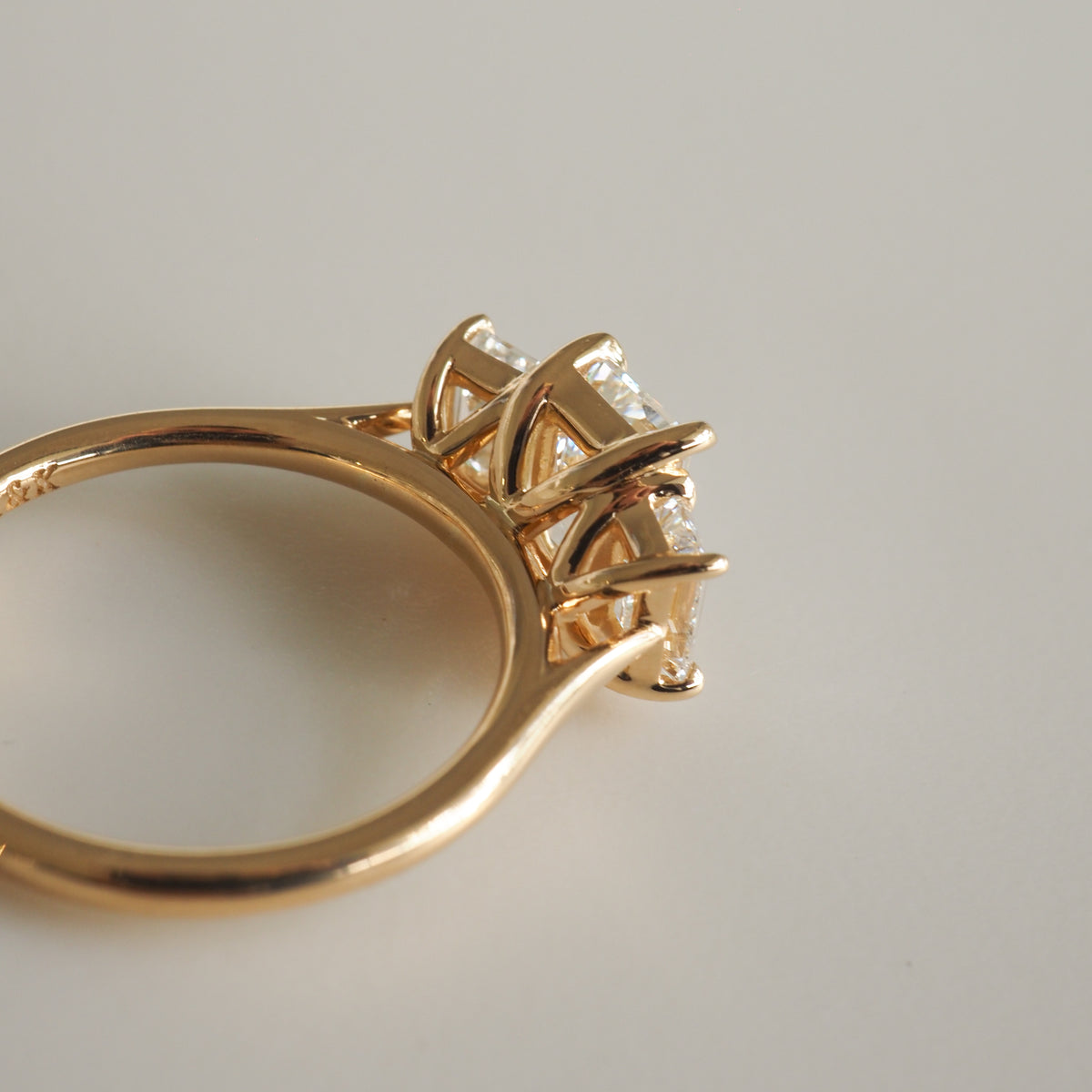 Gold engagement ring with a trio of sparkling diamonds set in elegant prongs, showcased on a smooth white surface.