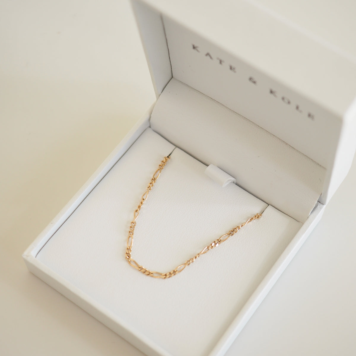 Delicate gold chain necklace in an open white Kate & Kole jewellery box, showcasing elegance and luxury craftsmanship.[text overlay: Medium Figaro]