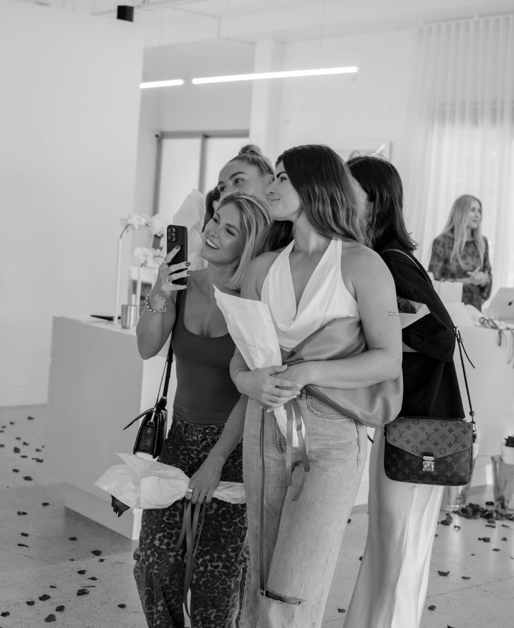Group of four women taking a selfie at a chic jewellery launch event, holding gift bags, surrounded by a stylish, modern interior.